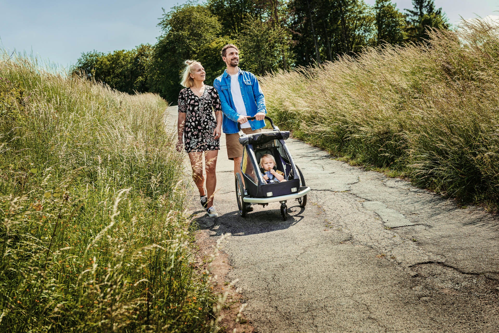 Happy mother and father going for a walk outside - child in Croozer Kid buggy with them